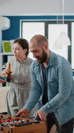 Man playing foosball game at table with woman and losing, having drinks after work. Colleagues meeting to drink beer and have fun with football game, enjoying free time after hoursの写真素材