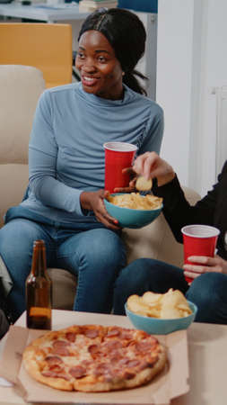 People enjoying drinks and snacks after work for leisure. Smiling coworkers with chips, pizza, and...