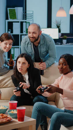 Multi ethnic group of people using joysticks to play video games on tv console for entertainment after work. Workmates playing game with controllers on television to do fun activity.の写真素材