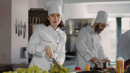 Portrait of female chef preparing celery ingredients for food dish, looking at camera. Woman in...
