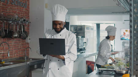 African american cooker looking at laptop screen to cook gourmet dish, following online food recipe...
