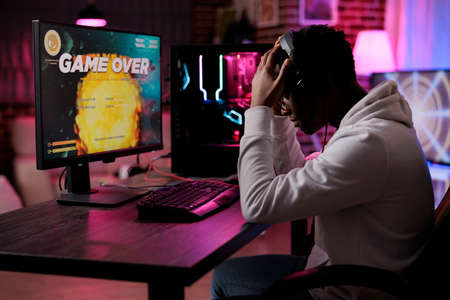 Frustrated young adult losing online video games play competition on computer with neon lights. Male...