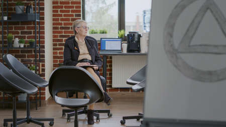 Psychologist sitting in circle with chairs and waiting on people at aa group meeting. Woman...
