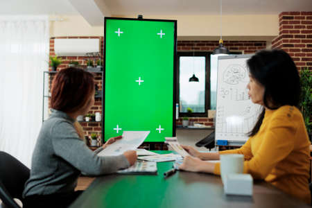 Women manager looking at green screen chroma key mock up vertical monitor with isolated display...