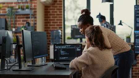 Two system engineers analyzing source code on laptop looking for errors on screen while sitting at desk. Team of app developers working on group project for ai online cloud computing project.の写真素材