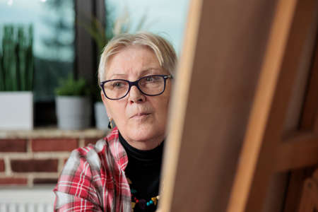 Portrait of elder painter teacher drawing sketch on graphic canvas during art courses in brick wall...