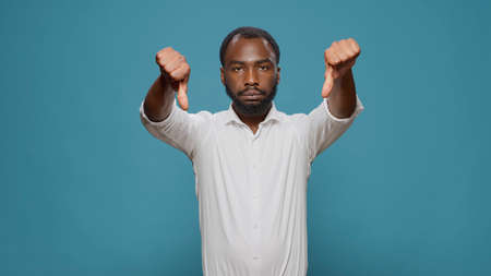 Displeased upset man showing thumbs down gesture, advertising rejection and disapproval about...