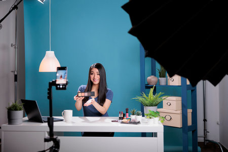 Behind the scene of social media creator holding make up palette doing cosmetic review while recording beauty podcast in studio. Asian woman advertising cosmetology product during live tutorialの写真素材
