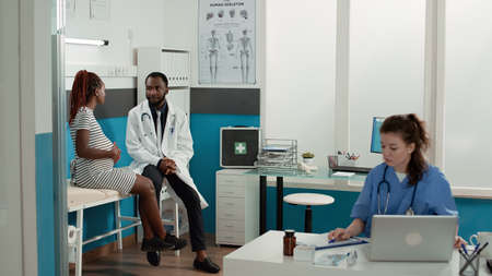 African american medic and pregnant patient meeting in cabinet to attend consultation appointment....