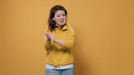 Happy casual woman clapping being supportive wearing hoodie over yellow background. Cool young adult...