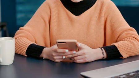 Cheerful woman browsing internet on smartphone at desk, doing college research and attending online...