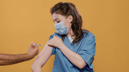 Portrait of medical doctor wearing surgical mask lifting sleeve and recieving covid or flu vaccine in studio. Medic wearing corona virus protection getting immunization shot from syringe.の写真素材