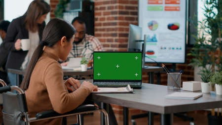 Businesswoman working in disability friendly office with greenscreen on display. Employee in...