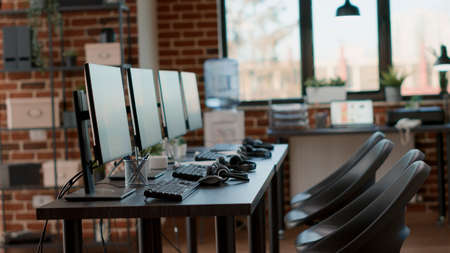 Nobody in customer service office with telemarketing technology, used to give support to helpline clients. Workstation with monitors, headphones and accessories at call center. Handheld shot.の写真素材
