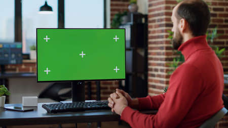 Male employee working with green screen on monitor, using technology at desk. Office worker analyzing blank copyspace with isolated mockup template and chroma key background on computer.の写真素材