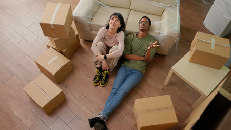 Pensive couple thinking about future in new apartment flat, sitting on living room floor and taking...