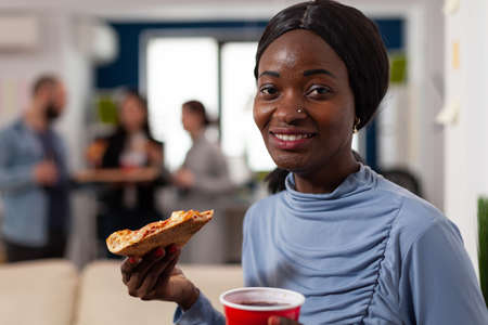 Portrait of african american woman holding pizza and beer, enjoying after work drinks party with...