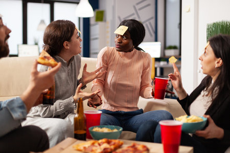 Multiethnic group of people play guessing game with sticky notes, laughing and having fun with drinks after hours. Office colleagues playing charades at party celebration with alcohol.の写真素材