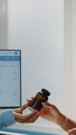 Close up of young patient receiving bottle of pills from doctor at annual checkup visit. Sick woman getting flask of medicine and prescription treatment from medic to cure illnessの写真素材