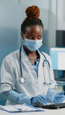 Medical specialist discussing healing treatment with ill woman in doctors office. Doctor doing medical consultation with patient while wearing face masks for protection against pandemicの写真素材