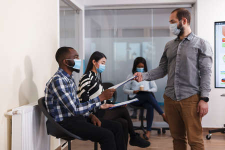 HR department manager receiving unemployed man CV resume in marketing company waiting room. African...