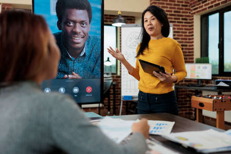 Entrepreneur explaining management strategy with remote manager during online videocall meeting conference in startup office. Business team working at company project. Teleconference call on monitorの写真素材