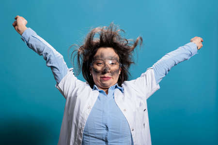 Funny looking scientist with messy hair and dirty face recovering from dangerous chemical explosion while stretching arms. Crazy and goofy looking laboratory chemist with smokey face and ugly hair.の写真素材