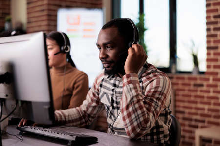 African american call center operator talking to clients on helpline, giving telemarketing assistance to people at customer care service. Helpdesk support consultant working at network reception.の写真素材