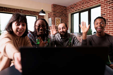 Multiracial people waving hand at online video conference on laptop while sitting at home. Diverse...