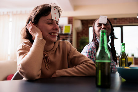 Smiling woman with card game on forehead enjoying society games with friends at home. Happy...