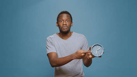Stressed man checking time on wall clock and running late to work, looking at hour and minutes....