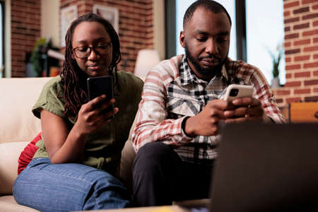 Boyfriend ignoring upset girlfriend after arguement spending time on smartphones sitting on couch....