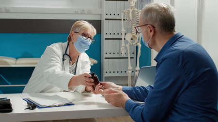 General practitioner and patient with face mask talking about pills bottle in medical office....