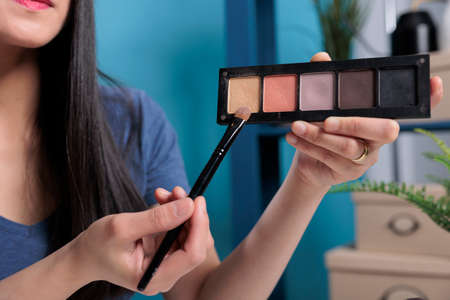 Beauty guru holding cosmetic palette showing at camera while filming make up tutorial reviewing...