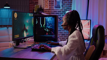 African american gamer girl using pc gaming setup playing multiplayer space shooter simulation having a good time in home living room. Woman streaming online action game while talking in headset.の写真素材