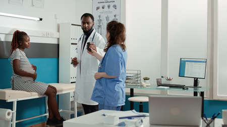 African american doctor giving bottle of pills to pregnant woman in health care service cabinet....