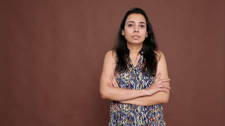 Portrait of indian woman posing with arms crossed on camera, standing over brown background. Young adult with positive expressions feeling confident and determined, proud person.の写真素材