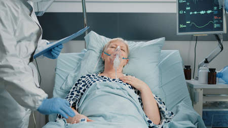 Paramedics consulting heavy breathing woman with oxygen tube in hospital ward quarantine. Doctor and...
