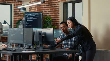 Two software developers holding laptop with coding interface walking towards desk and sitting down...