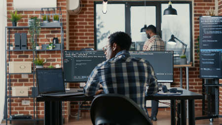 Programer coding on laptop sitting down at desk with computer screens parsing code in software...
