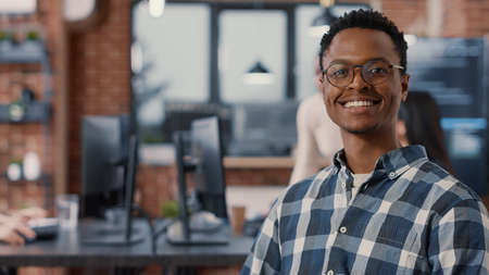 Portrait of app developer sitting down looking at laptop screen and looking up smiling at camera in...