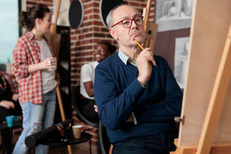 Portrait of elderly student drawing vase on white canvas sketching model using graphic pencil in...