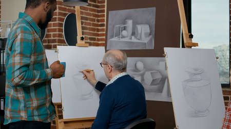 Young teacher helping senior man with vase masterpiece, teaching new drawing skills in art class. Elder student attending artistic lesson to learn technique for educational development.の写真素材