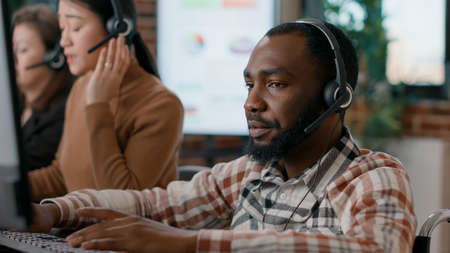 Young man answering telework call at customer service job, talking to clients on phone helpline. Male worker using audio headset to given assistance and support to people. Close up.の写真素材