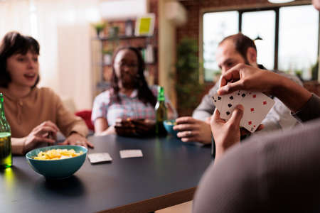 Selective focus of african american man holding cards while playing with best friends at home. Happy...