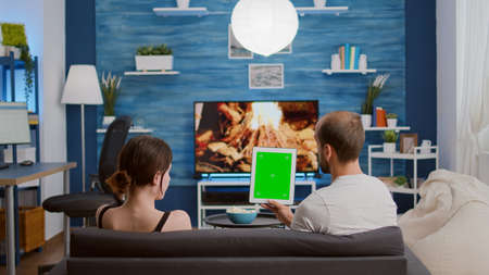 Static tripod shot of couple holding vertical digital tablet with green screen talking about influencer vlog content. Man and woman using touchscreen device with chroma key watching social media.の写真素材