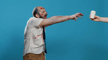 Angry ugly zombie trying to get cup of coffee on blue background. Dangerous apocalypse brain dead...