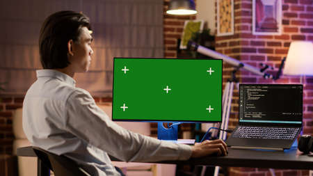 Male entrepreneur using computer display with greenscreen to work on business. Looking at isolated...