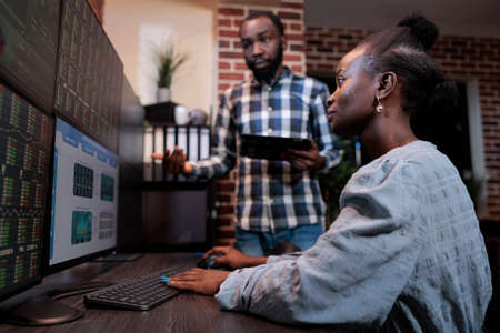 Sales consultant sitting at multi monitor workstation while coworker having touchscreen tablet device. Hedge fund traders discussing about market live graph and real time financial data.の写真素材
