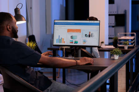 African american worker analyzing business charts with data on computer screen, using online...